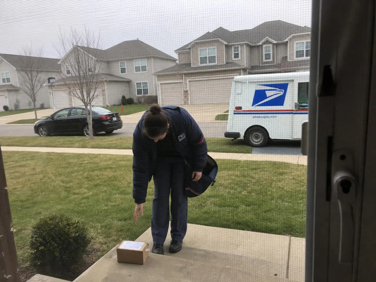 USPS Priority Mail carrier handing a package to a customer in an American neighborhood