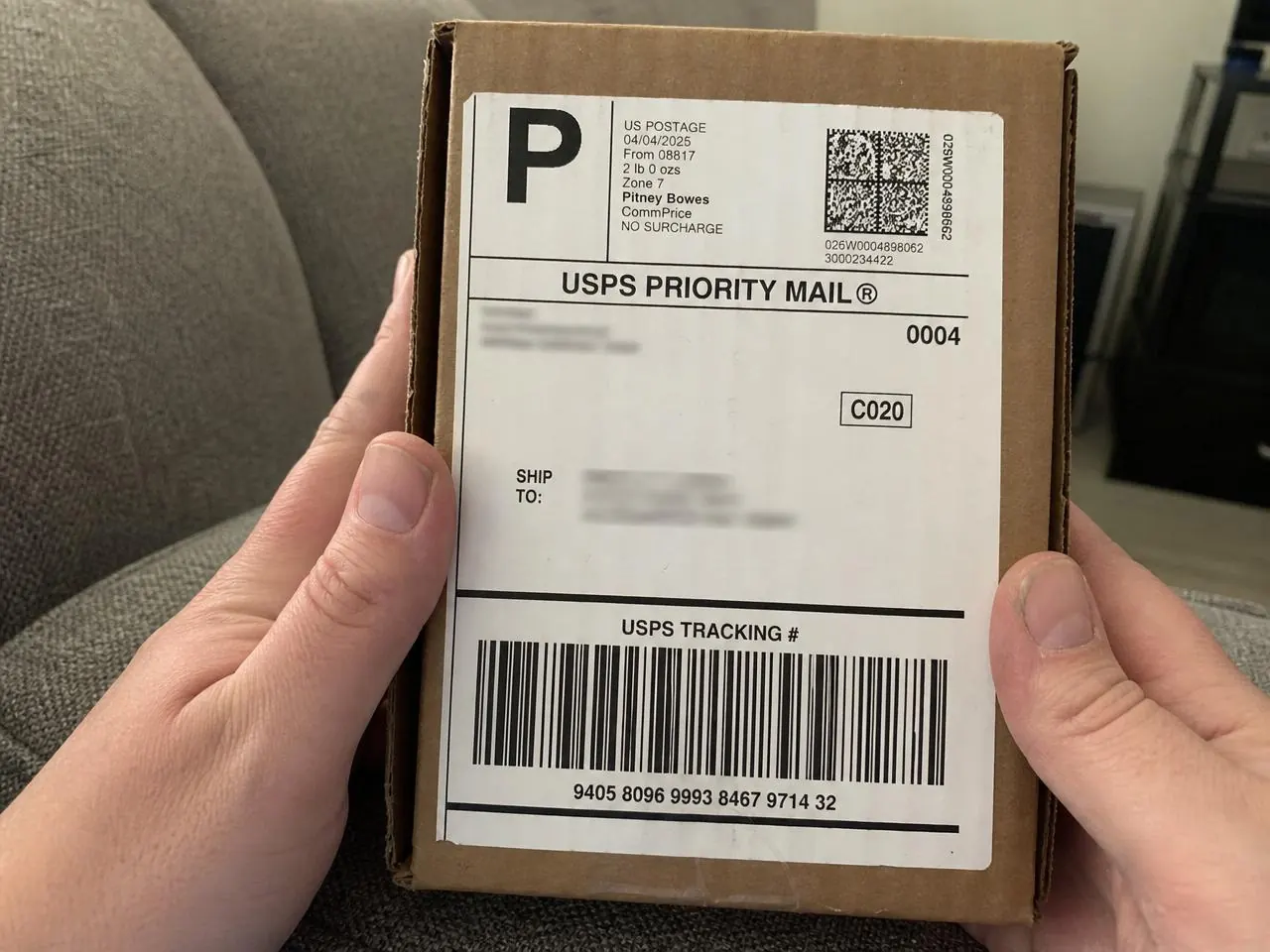 Customer holding a small USPS Priority Mail package with a clear tracking label